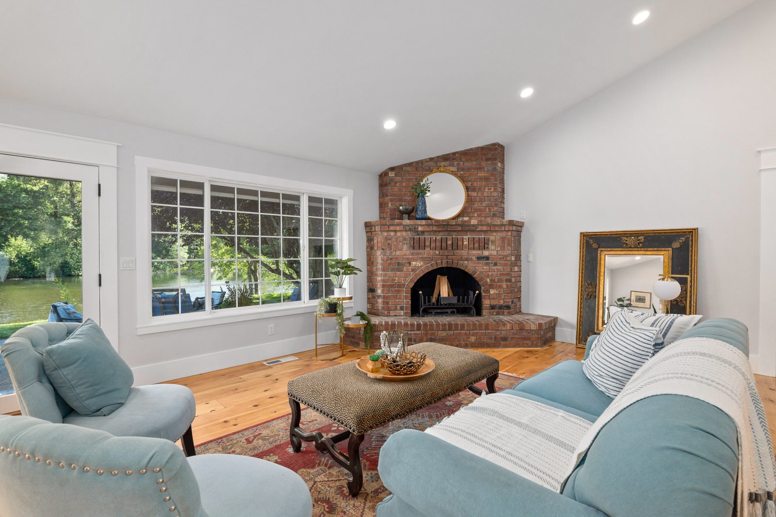 Living room with a brick corner fireplace, vaulted ceiling, and wide-plank wood floors