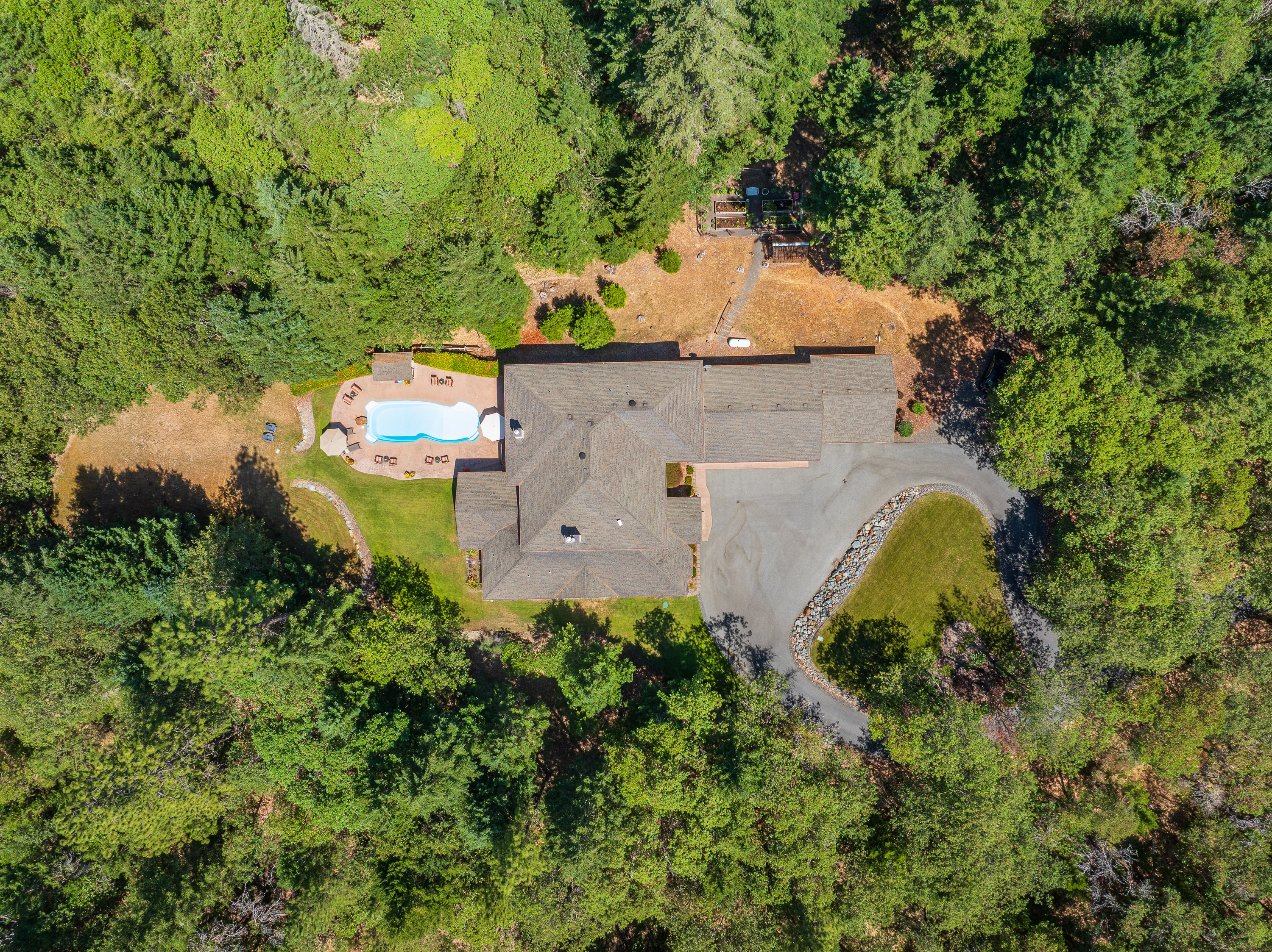 Aerial view of a Southern Oregon home with cleared lawn and hardscape around the structure, surrounded by dense fir and oak forest — defensible space in practice.