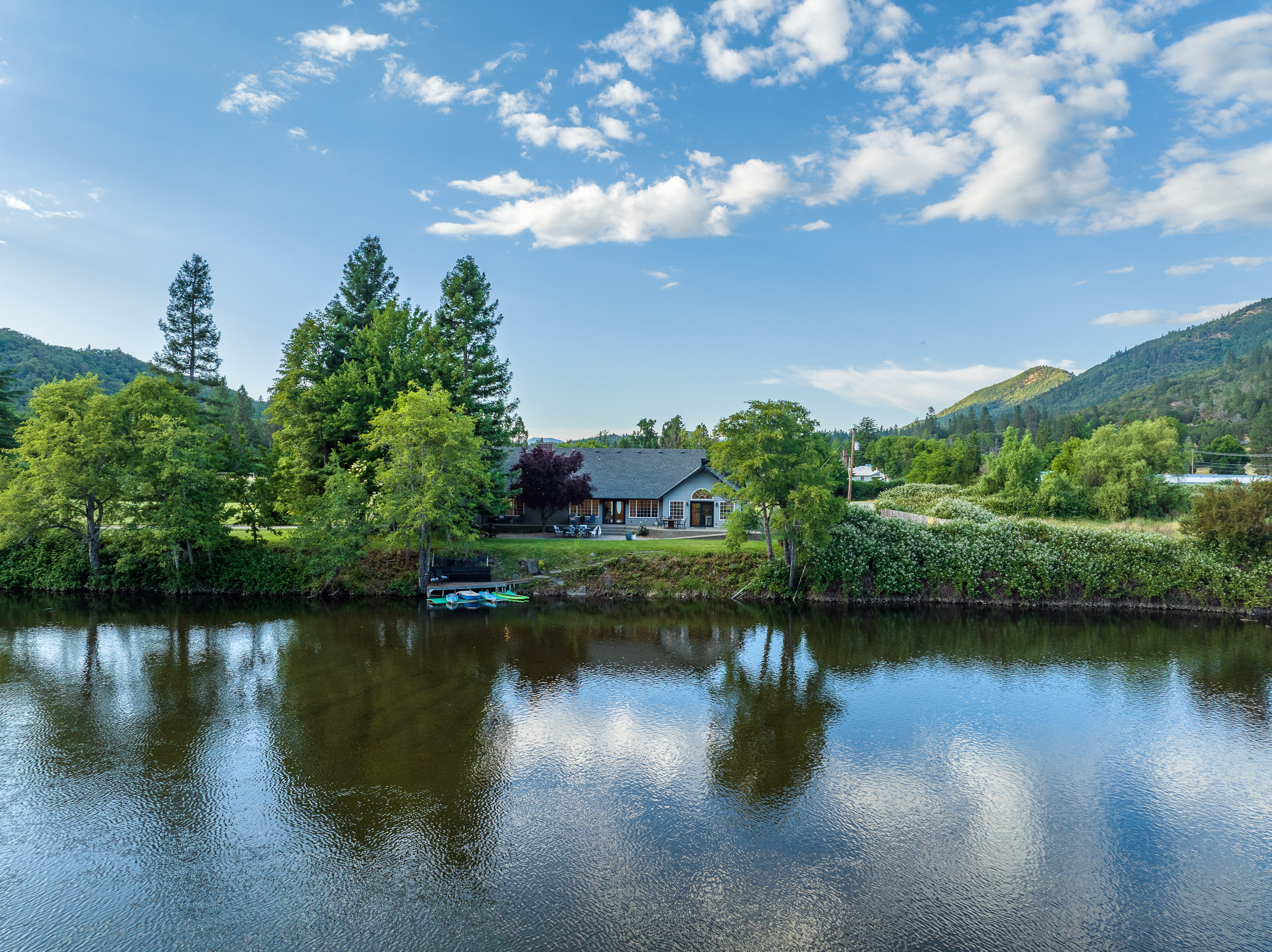 Calm evening water on the Rogue River in Josephine County, Oregon, with a private dock and kayaks along a wooded bank.